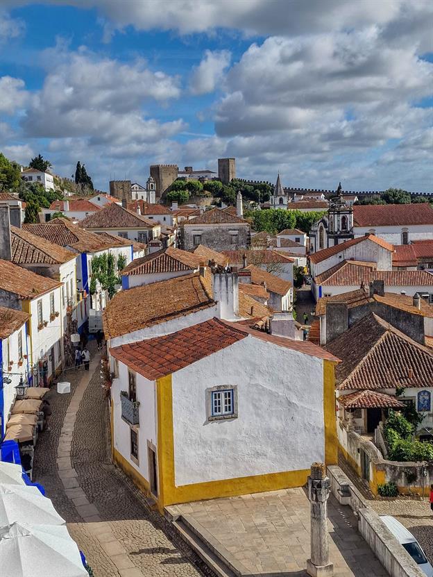 Óbidos, ein bezauberndes mittelalterliches Städtchen in Portugal, liegt eingebettet in eine malerische Landschaft und ist von einer gut erhaltenen Stadtmauer umgeben. Mit seinen kopfsteingepflasterten Gassen, weiß getünchten Häusern, die mit Bougainvillea geschmückt sind, und dem imposanten Schloss, das über dem Ort thront, fühlt man sich wie in eine Märchenwelt versetzt. Besonders charmant ist die Tradition, den Besuchern einen Schluck Ginja, einen lokalen Kirschlikör, in kleinen Schokoladentassen zu servieren. 
(05.2024)