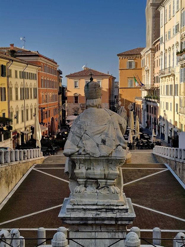 Stell dir den Piazza del Plebiscito vor: ein lebendiger Platz, umringt von historischen Gebäuden, Cafés und einem Hauch von italienischem Chaos. Mitten drin thront eine Statue, die gelassen auf das Treiben blickt – vermutlich denkt sie sich: „Meine Güte, diese Menschen und ihre Espressos!“ Die Figur, Papa Clemens XII, steht da wie ein geduldiger Beobachter, der schon seit Jahrhunderten zusieht, wie die Anconitaner über den Platz eilen, plaudern und gestikulieren. Vielleicht wartet sie auch nur darauf, dass endlich jemand ihr einen Cappuccino bringt. Ein echter Platz-Hipster, der schon cool war, bevor cool überhaupt erfunden wurde. 😎
(12.2024)