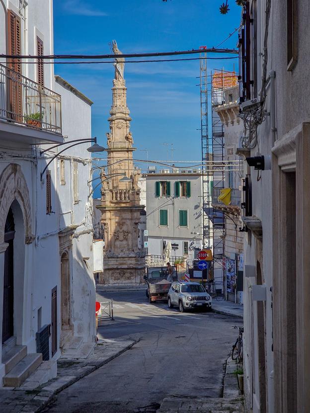 In Ostuni gibt es eine imposante Statue des Heiligen Oronzo, der auf seinem Sockel hoch oben thront und mit weisem Blick über die Stadt wacht. Man könnte fast meinen, er beobachte jeden Bissen, den man von seinem Gelato nimmt! Der Heilige Bischof, mit seiner erhobenen Hand, sieht aus, als wollte er den vorbeigehenden Touristen segnen oder ihnen vielleicht sogar eine freundliche Erinnerung geben, dass sie nicht vergessen sollen, ihre Sonnencreme aufzutragen.
(01.2025)